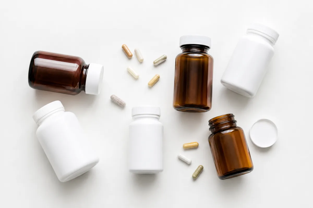 Several unlabeled amber and white supplement bottles with loose capsules scattered on a bright white surface