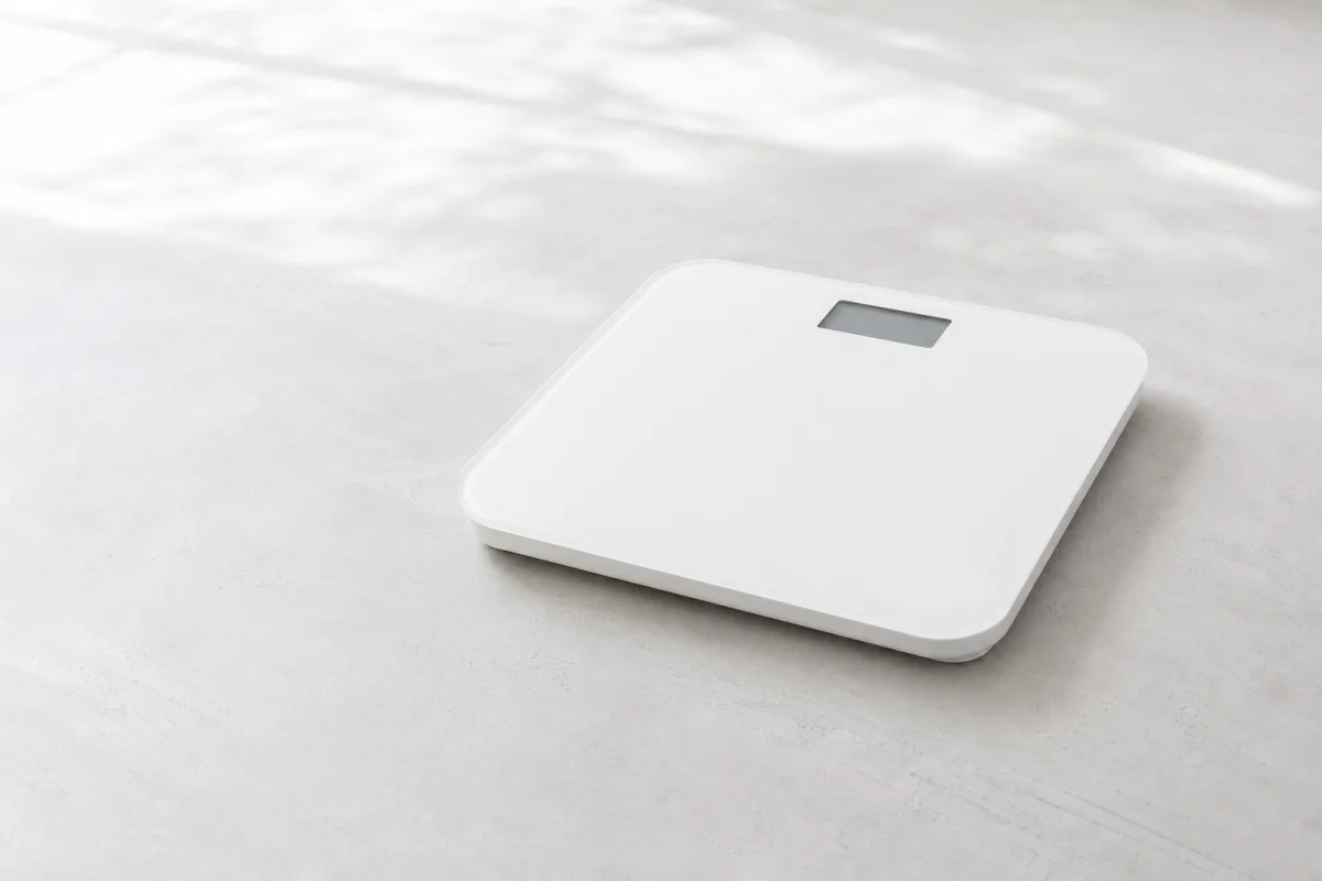 A plain white bathroom scale on a bright pale floor with a blank display