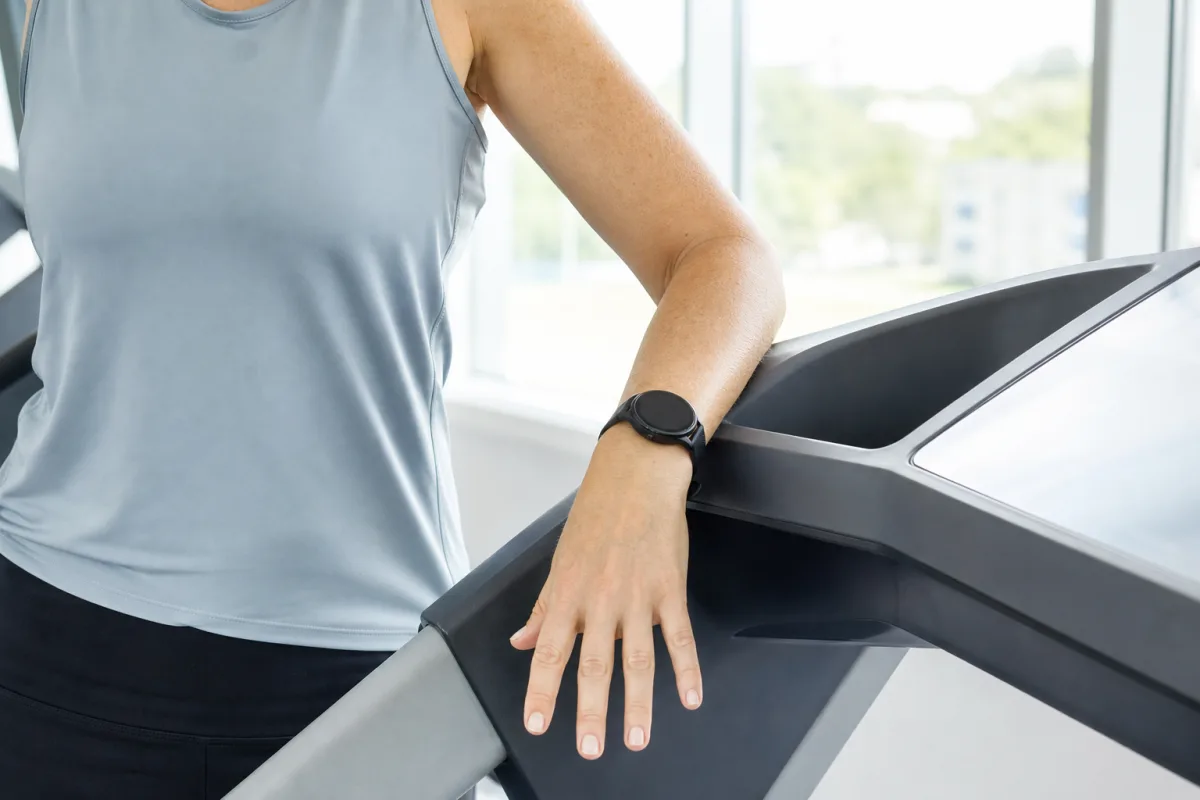 A woman's forearm resting on a treadmill console after a workout, wearing a fitness watch